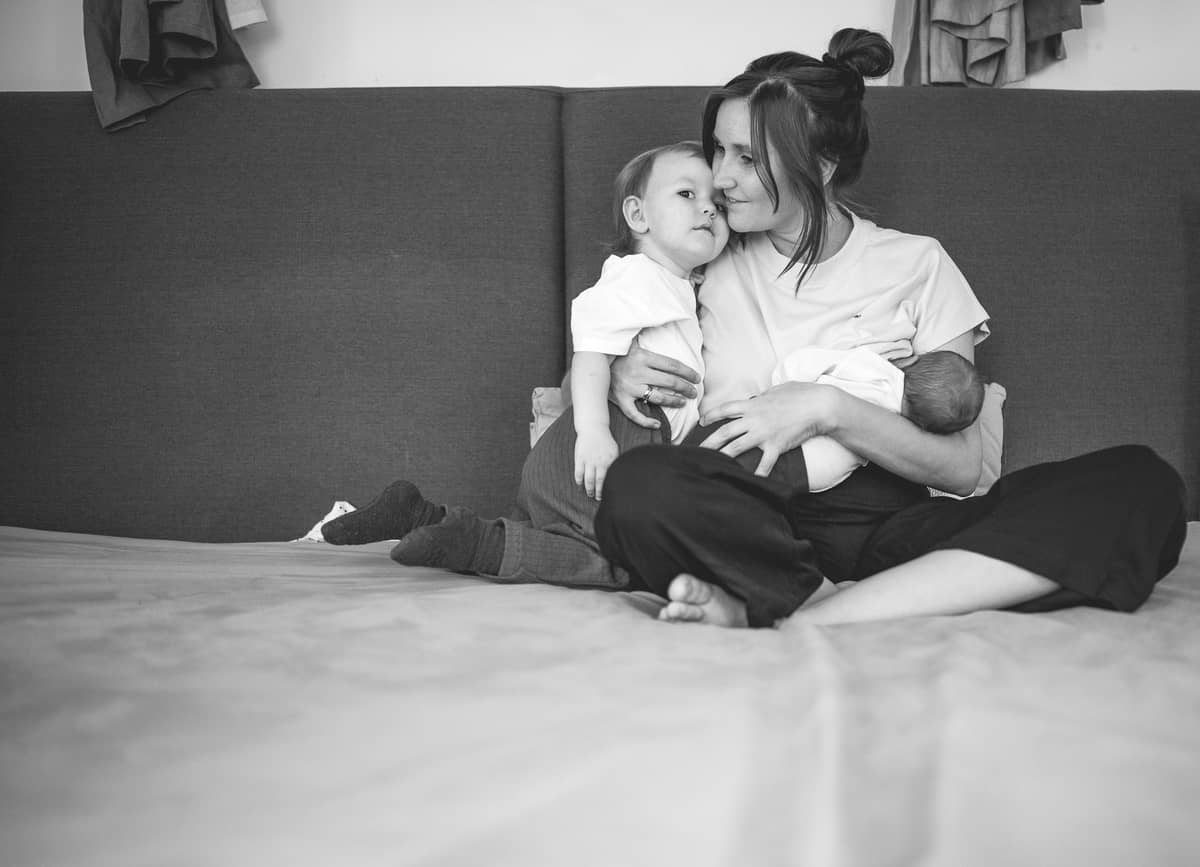 Schwarzweißbild einer Mama mit Kleinkind und Neugeborenem auf dem Bett