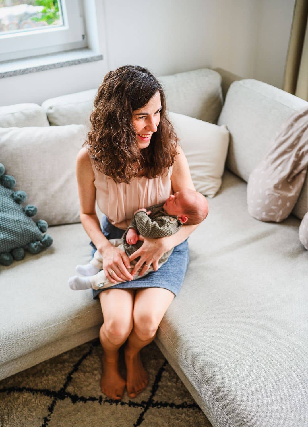 Mama sitzt mit ihrem Baby im Arm auf dem Sofa