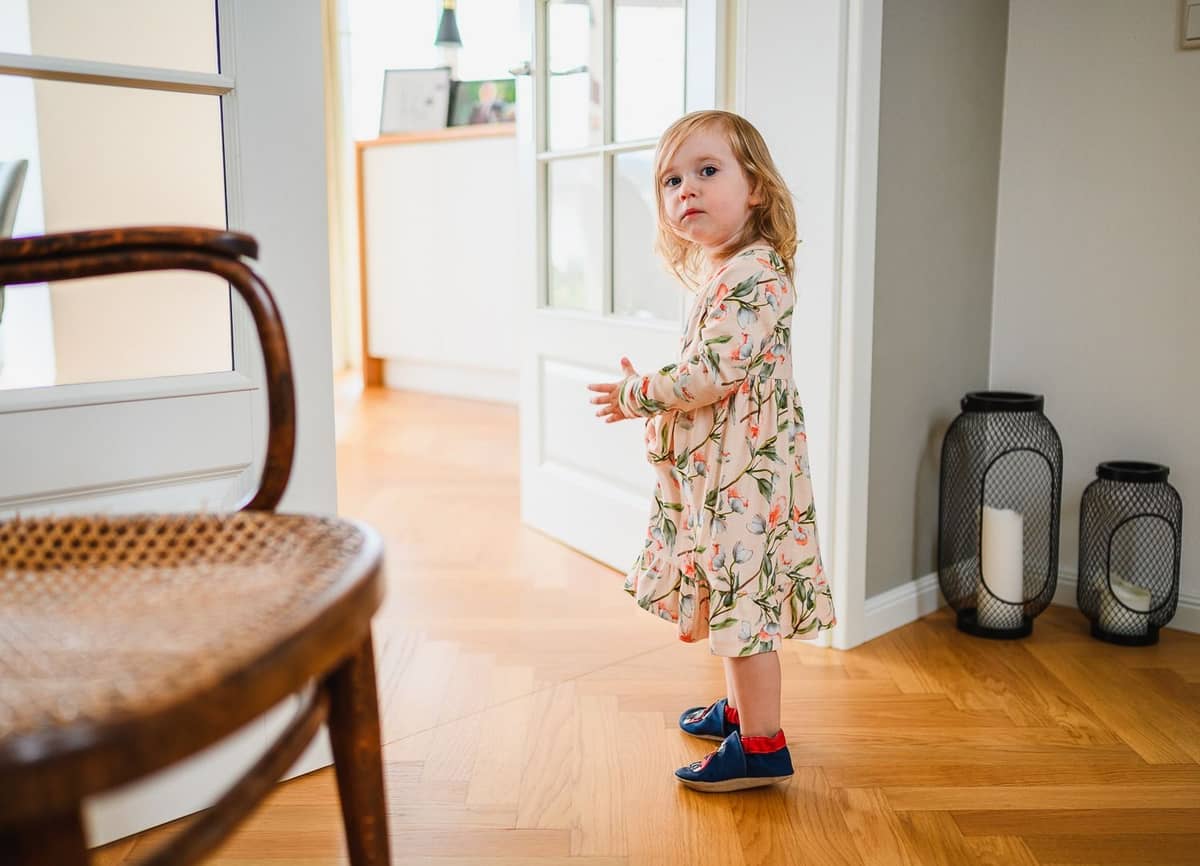 Kleines Mädchen im geblümten Kleid steht im hellen Flur