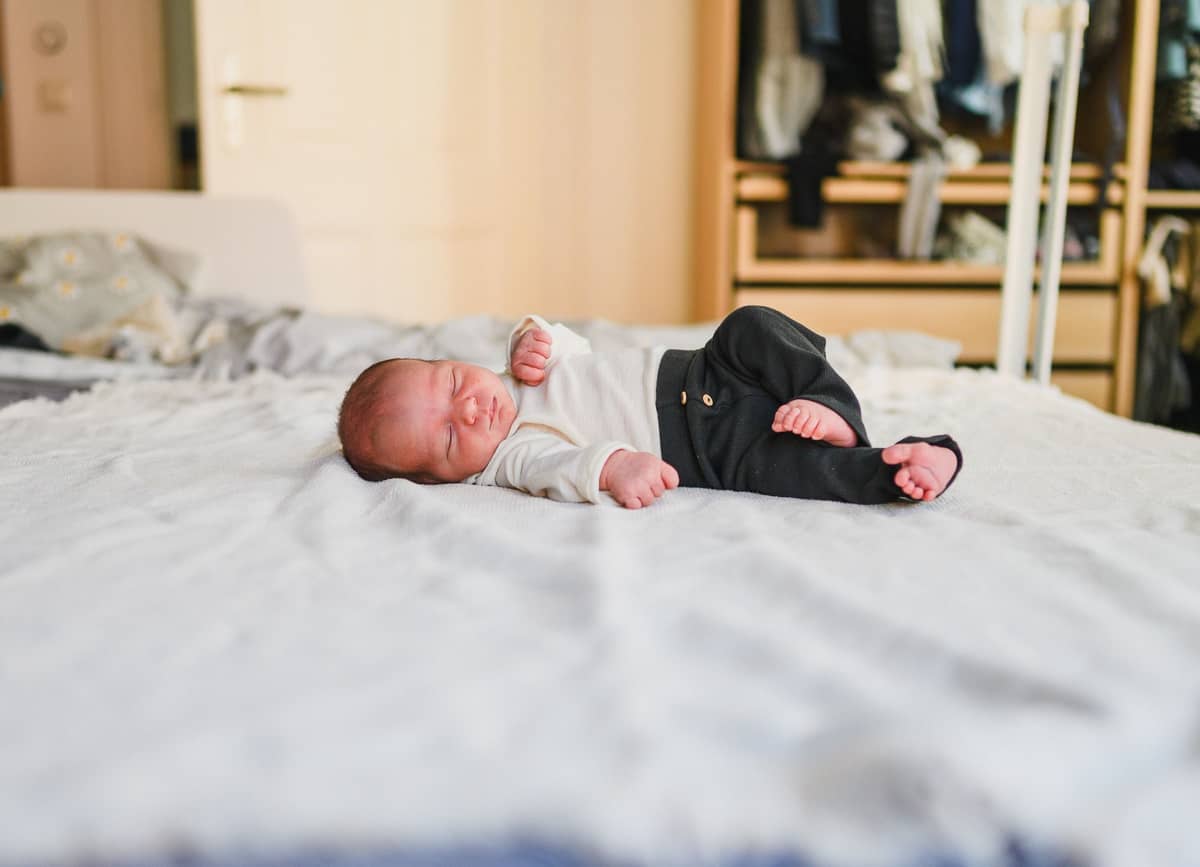 Neugeborenes liegt auf dem großen Bett im Schlafzimmer der Familie