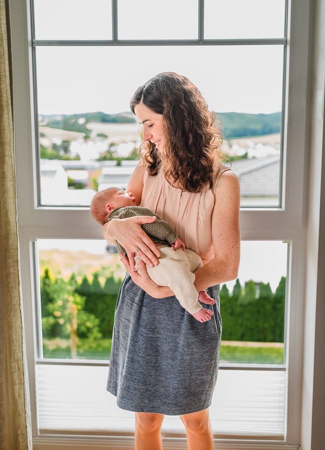 Mama steht mit ihrem Neugeborenen im Arm vor einem großen Fenster