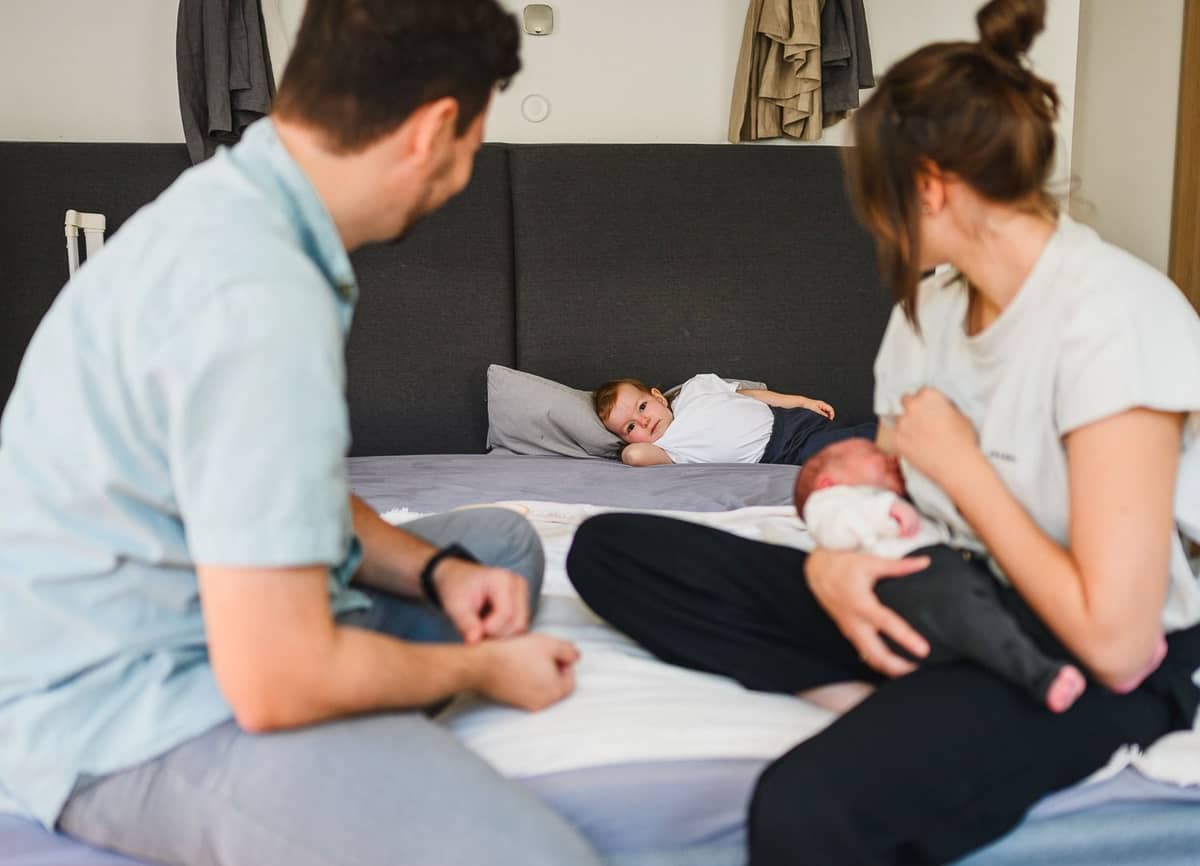 Eltern sitzen mit ihrem Neugeborenen auf dem Bett