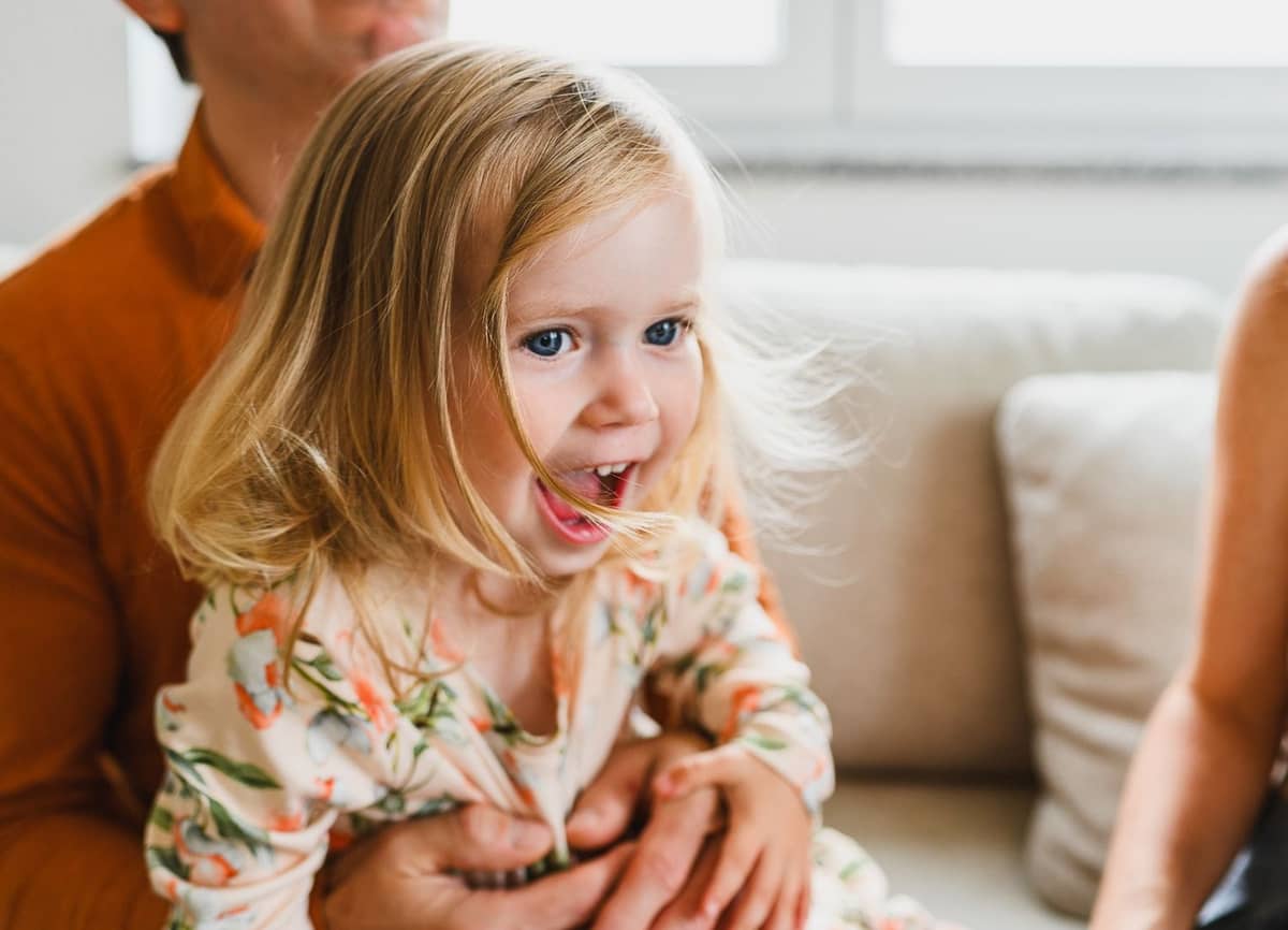 Kleines Mädchen im geblümten Kleid lacht auf dem Schoß ihres Papas