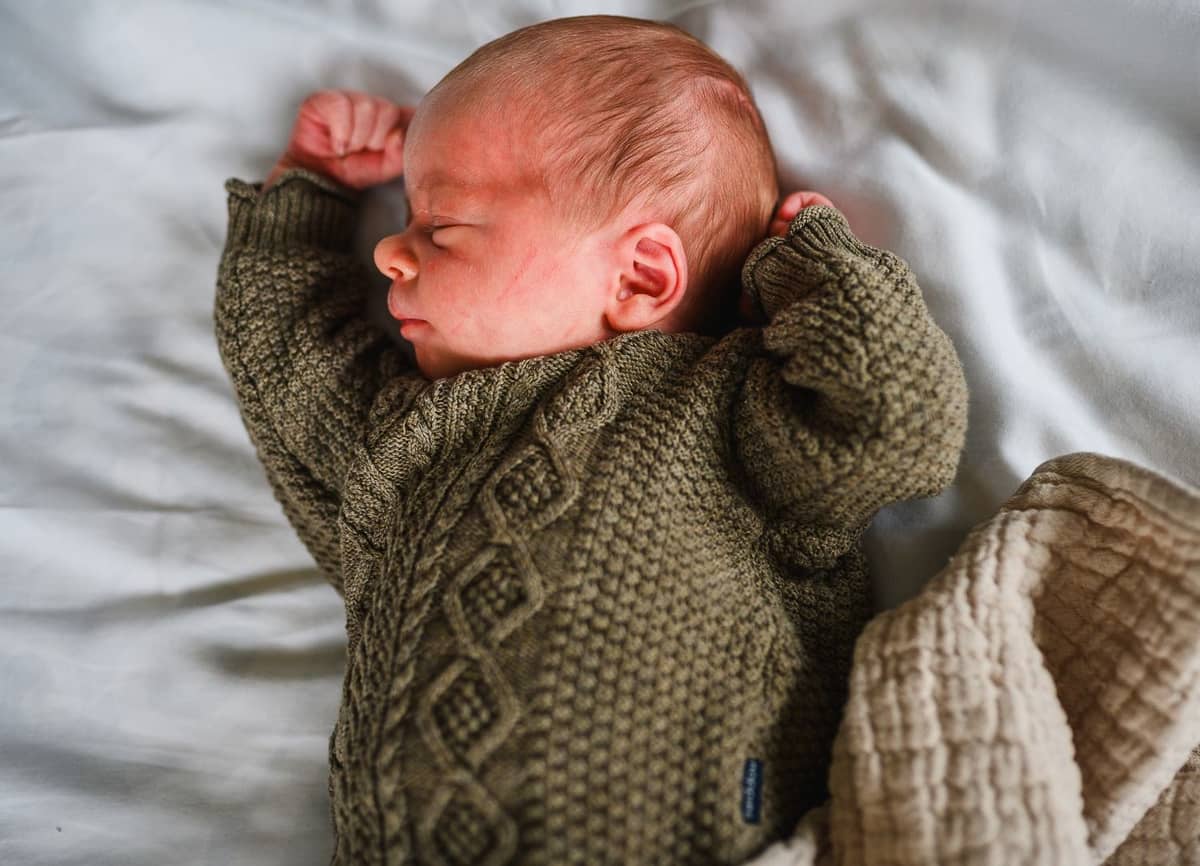 Neugeborenes im grünen Strickpullover schläft auf einer weißen Decke