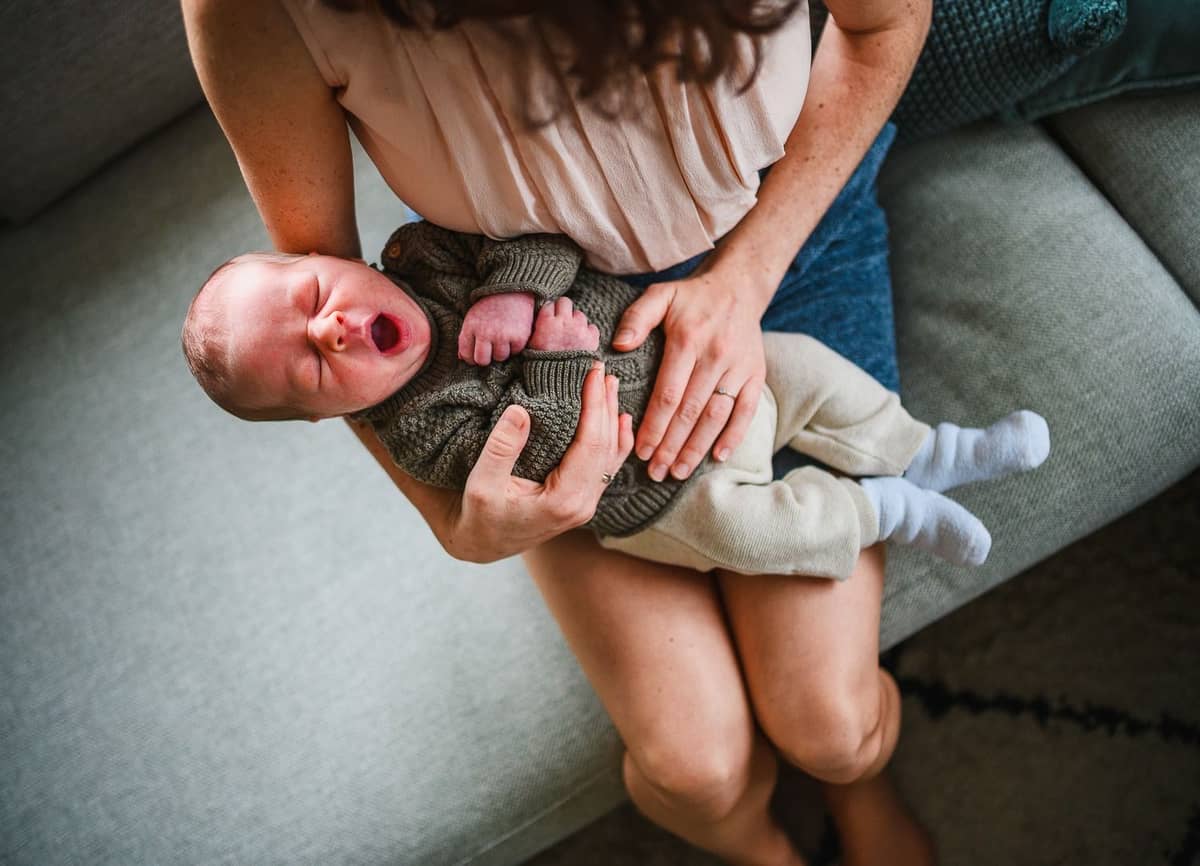 Mama hält ihr gähnendes Neugeborenes auf dem Schoß