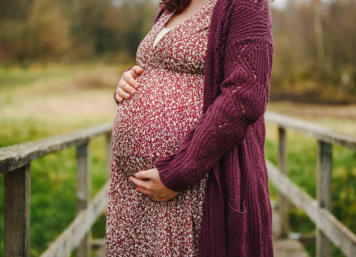 Nahaufnahme vom Babybauch im geblümten Kleid an einer Holzbrücke
