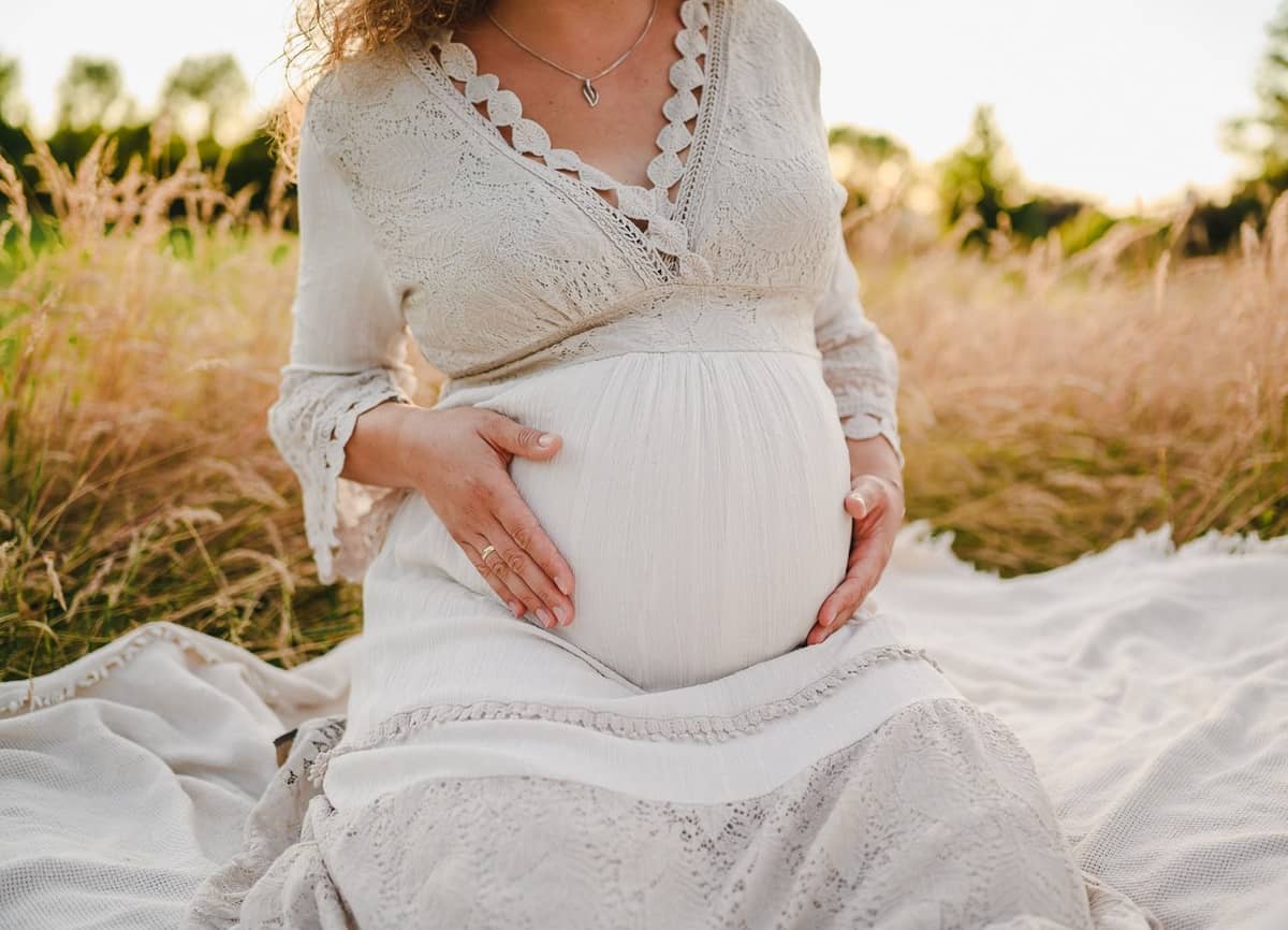 Hände auf dem Babybauch im weißen Spitzenkleid