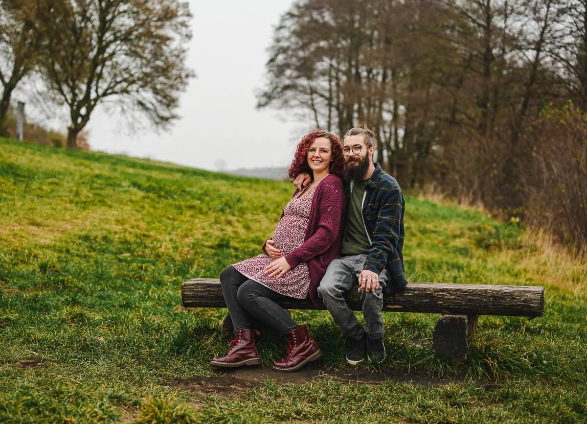 Werdende Eltern sitzen auf einer Holzbank auf einer grünen Wiese
