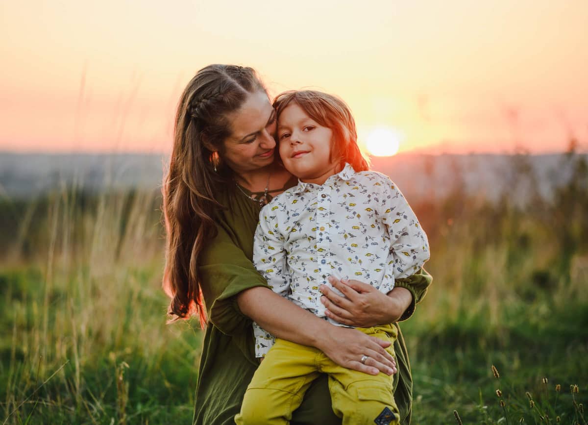 Mama hält ihren Sohn liebevoll im Arm, im Hintergrund geht die Sonne unter