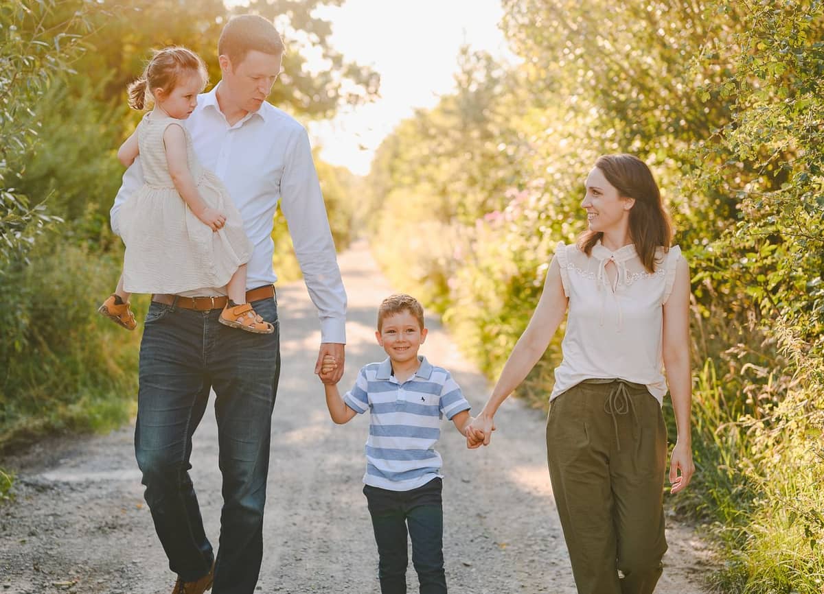 Familie mit zwei Kindern geht einen sonnigen Feldweg entlang