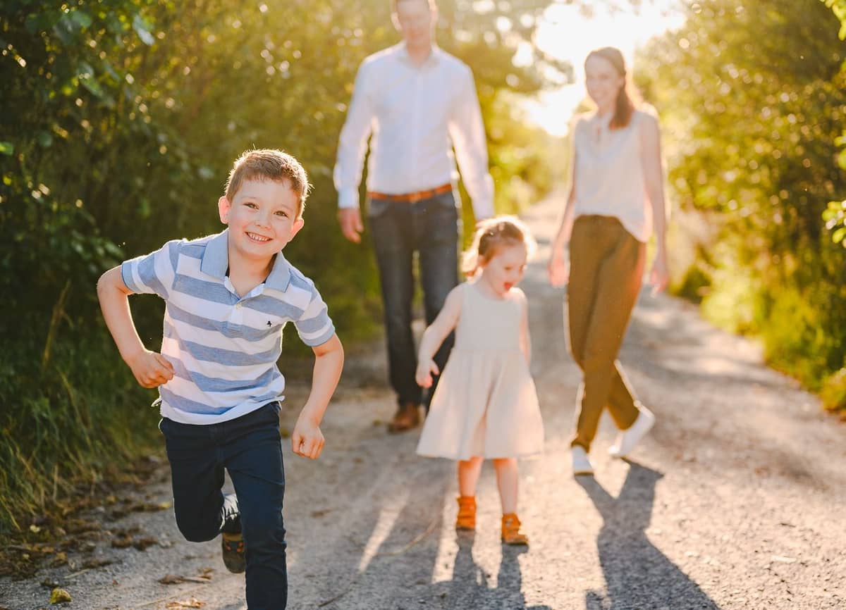 Familie spaziert einen sonnigen Weg entlang, der Sohn rennt voraus