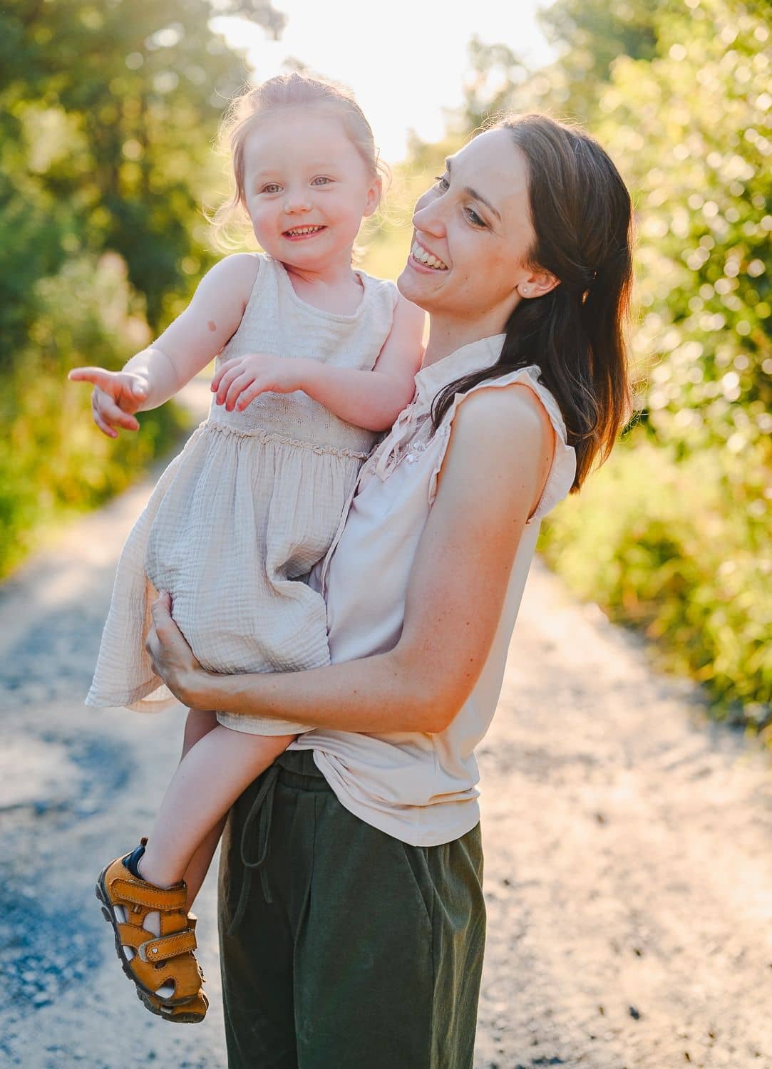 Mama trägt ihre lachende Tochter auf einem sonnigen Weg
