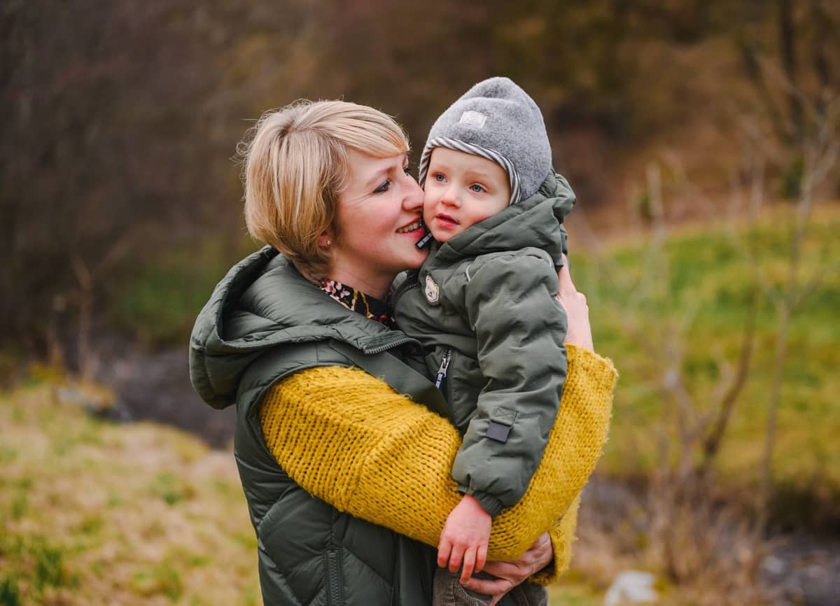 Mama mit ihrem lachenden Kleinkind auf dem Arm bei einem Herbstspaziergang