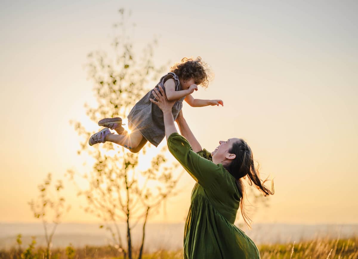 Mama wirbelt ihre kleine Tochter im Gegenlicht der Abendsonne durch die Luft