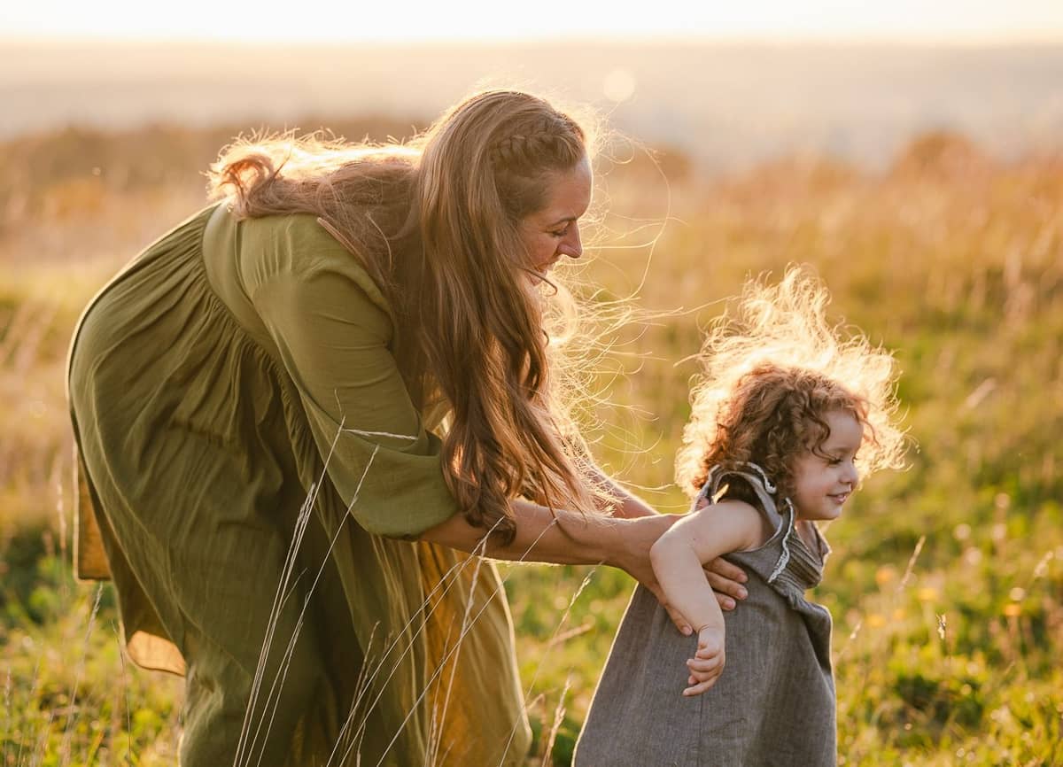 Mama spielt mit ihrer Tochter im hohen Gras bei Sonnenuntergang