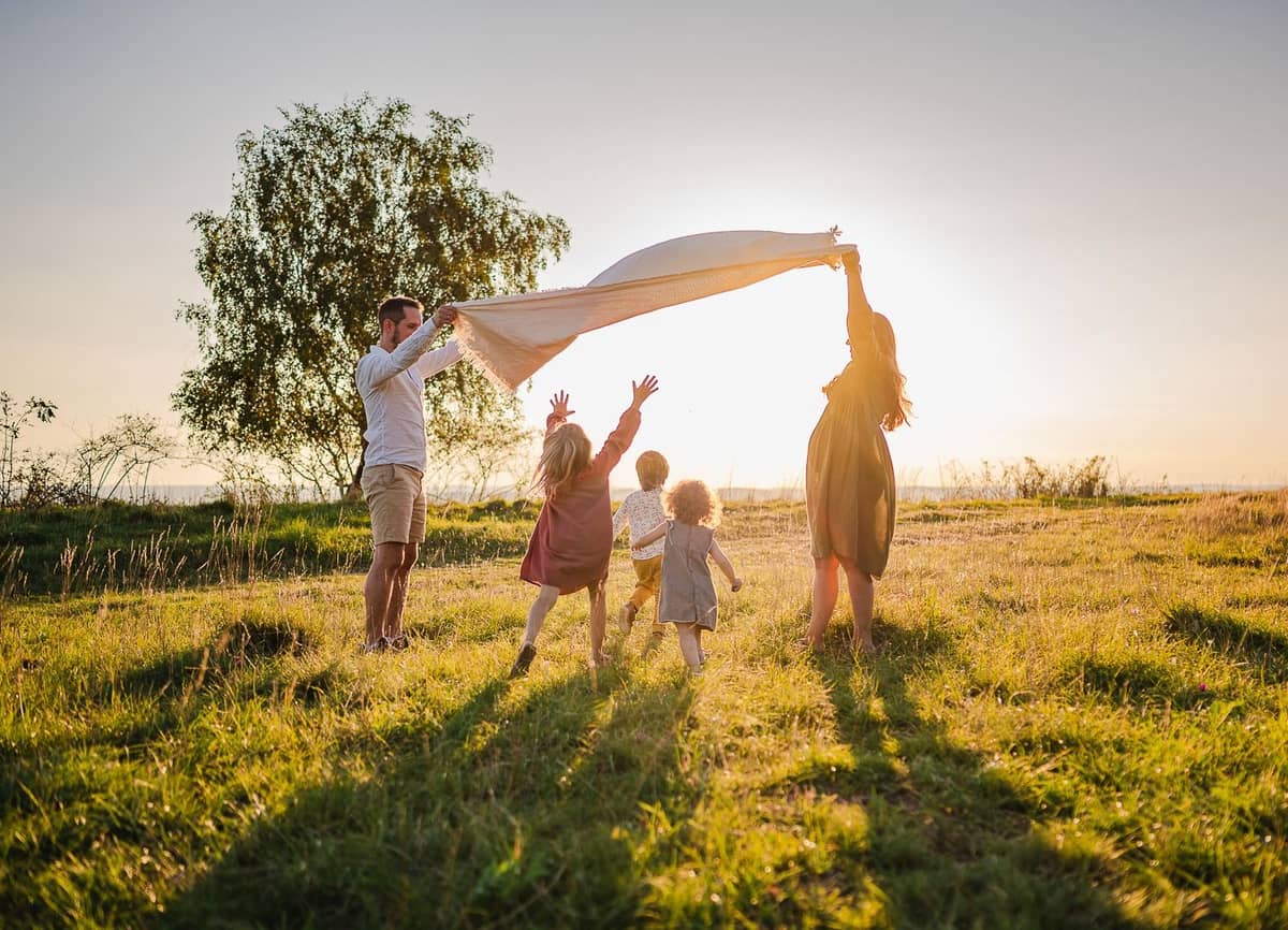 Familie spielt mit einem Tuch auf der Wiese im Gegenlicht