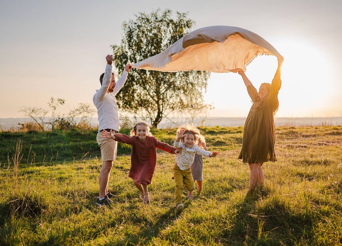 Familie hält ein großes Tuch in den Wind, die Kinder laufen darunter