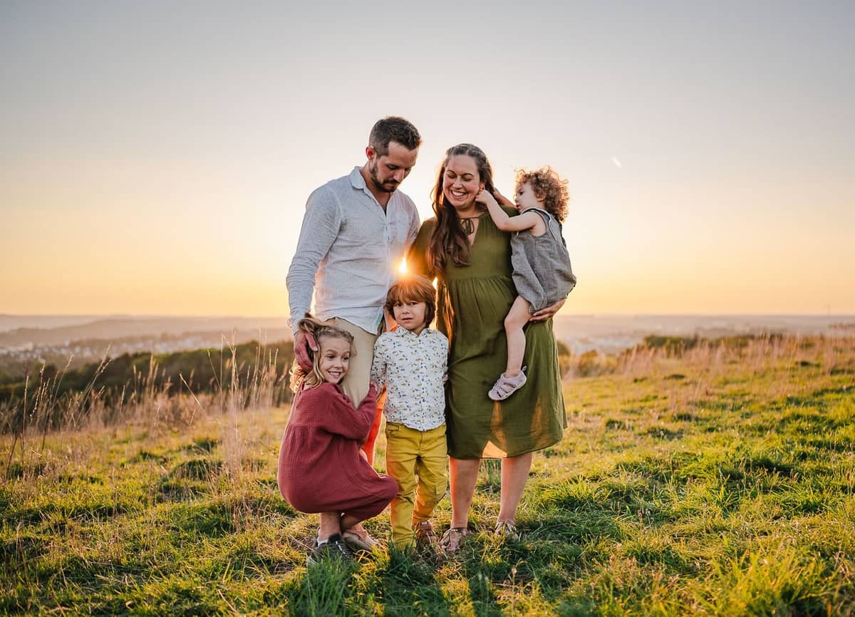 Familie mit drei Kindern steht lachend auf einer Wiese bei Sonnenuntergang