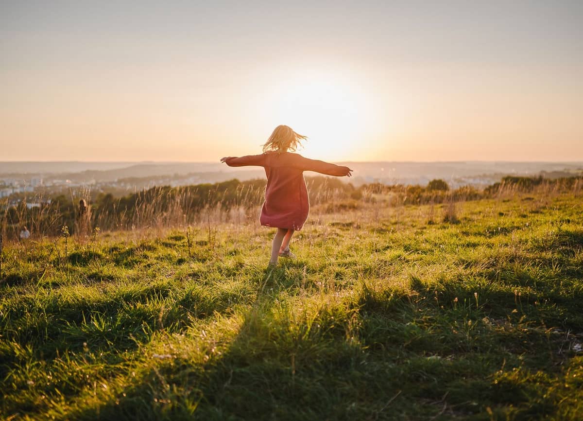 Mädchen im roten Kleid tanzt mit ausgebreiteten Armen im Sonnenuntergang